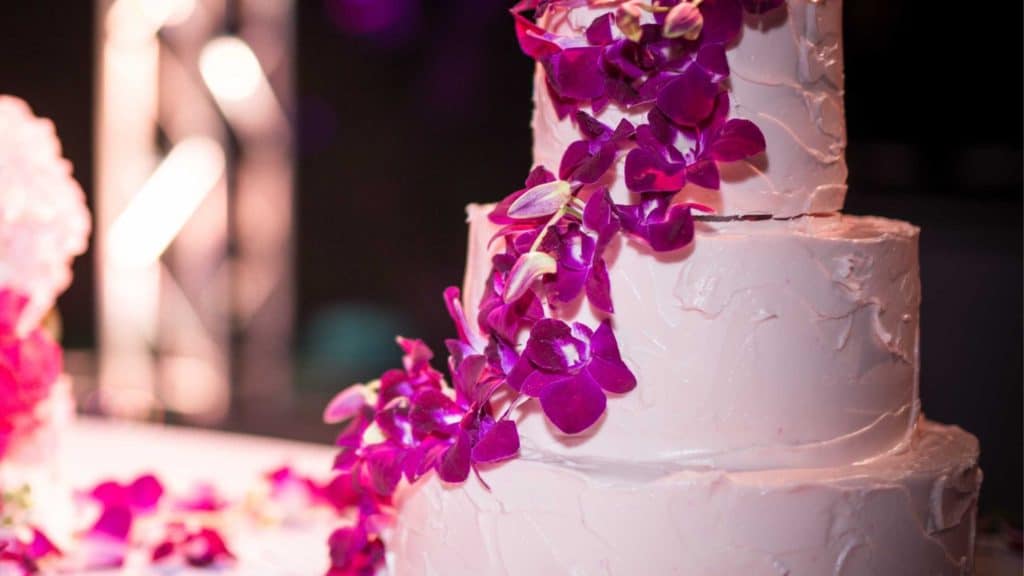 White tiered wedding cake with fuchsia colored flowers 